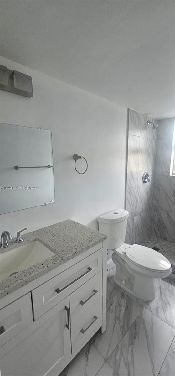 full bath featuring vanity, toilet, tiled shower, and marble finish floor