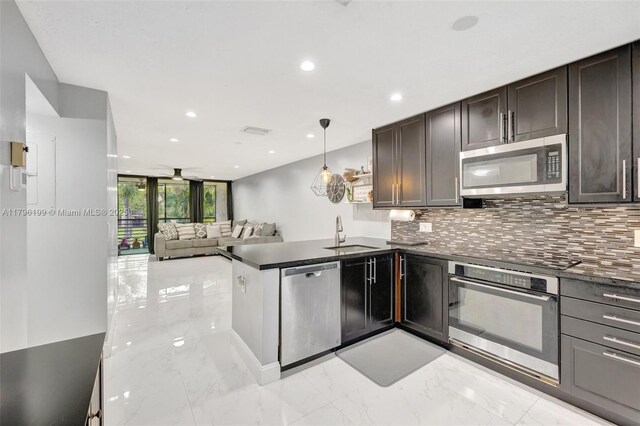 kitchen with a peninsula, a sink, dark countertops, appliances with stainless steel finishes, and tasteful backsplash