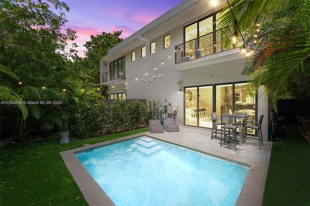 3132 Plaza St, Miami, FL 33133 - back of property at dusk featuring a balcony, stucco siding, a patio, and an outdoor pool