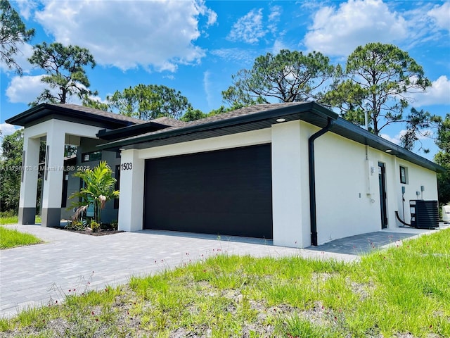 view of front of property featuring decorative driveway, stucco siding, central AC unit, and a garage