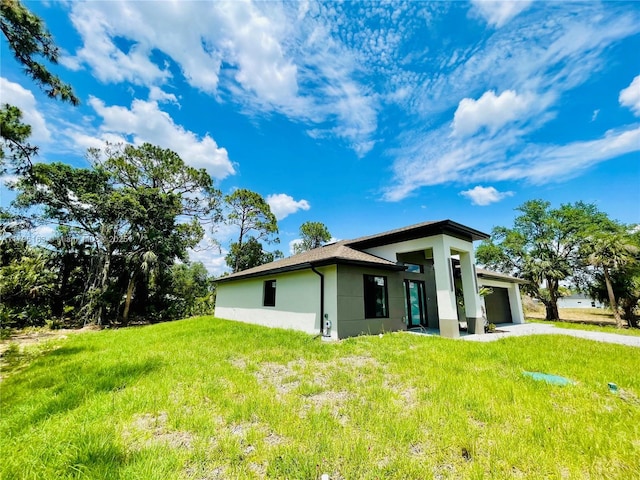 back of house featuring a yard, an attached garage, stucco siding, and driveway