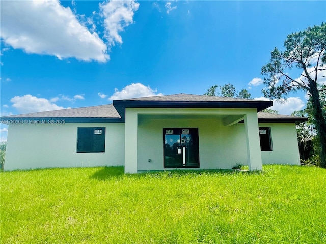 rear view of house featuring a lawn and stucco siding