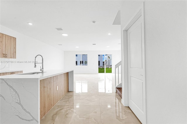 interior space featuring recessed lighting, a kitchen island with sink, marble finish floor, and a sink