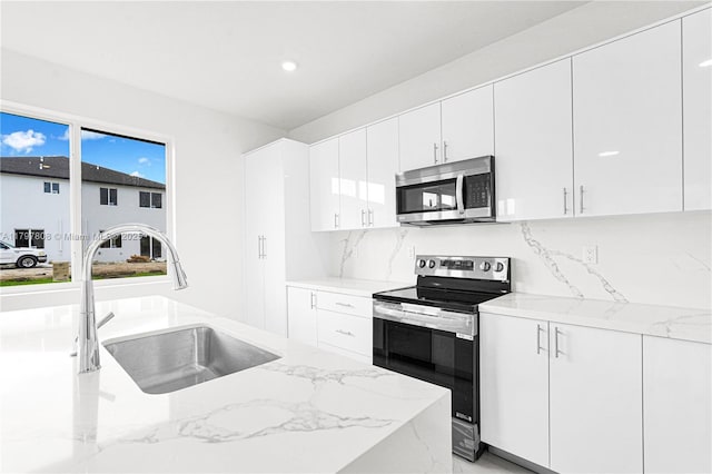 kitchen featuring a sink, white cabinets, backsplash, appliances with stainless steel finishes, and light stone counters