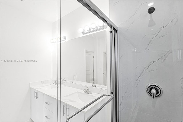full bath with double vanity, a marble finish shower, and a sink