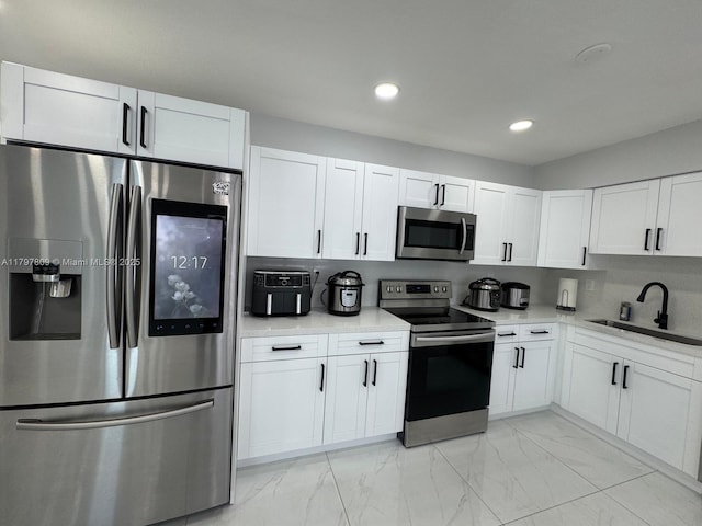 kitchen with marble finish floor, a sink, white cabinetry, light countertops, and appliances with stainless steel finishes