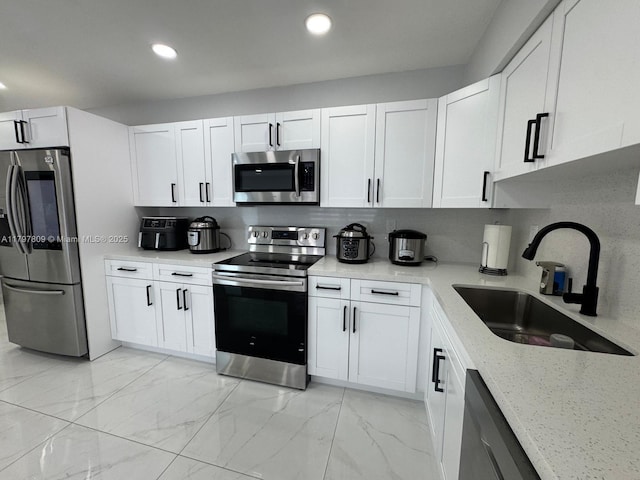 kitchen featuring marble finish floor, a sink, stainless steel appliances, white cabinets, and light stone counters