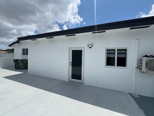 rear view of house with a patio area, stucco siding, and ac unit