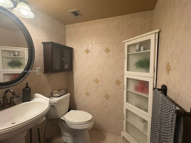 half bath featuring toilet, tile walls, visible vents, and a sink