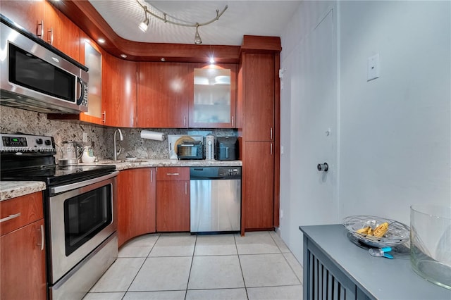5838 Collins Ave Unit 10E, Miami Beach, FL 33140 - kitchen featuring stainless steel appliances, decorative backsplash, light tile patterned floors, brown cabinetry, and glass insert cabinets