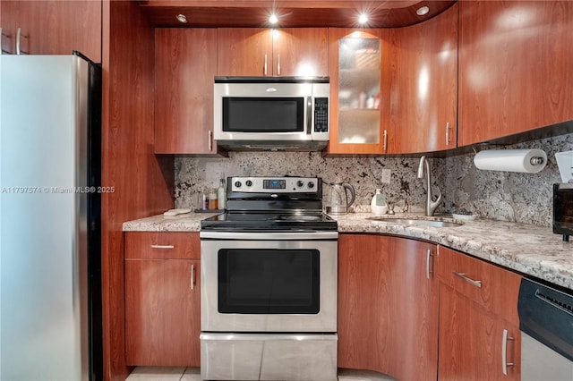 5838 Collins Ave Unit 10E, Miami Beach, FL 33140 - kitchen with stainless steel appliances, brown cabinets, light stone countertops, decorative backsplash, and glass insert cabinets