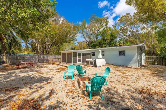 rear view of property featuring a sunroom, a fire pit, and a fenced backyard