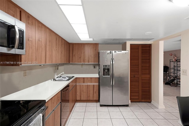 kitchen with light tile patterned floors, brown cabinetry, a sink, light countertops, and appliances with stainless steel finishes