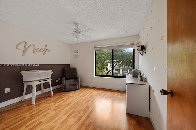 sitting room with light wood-style flooring, ceiling fan, and a textured ceiling