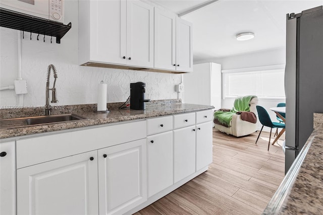 kitchen with a sink, freestanding refrigerator, white cabinets, light wood finished floors, and stone counters