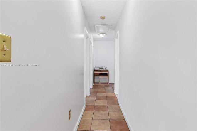 hall with a textured ceiling, baseboards, and light tile patterned floors