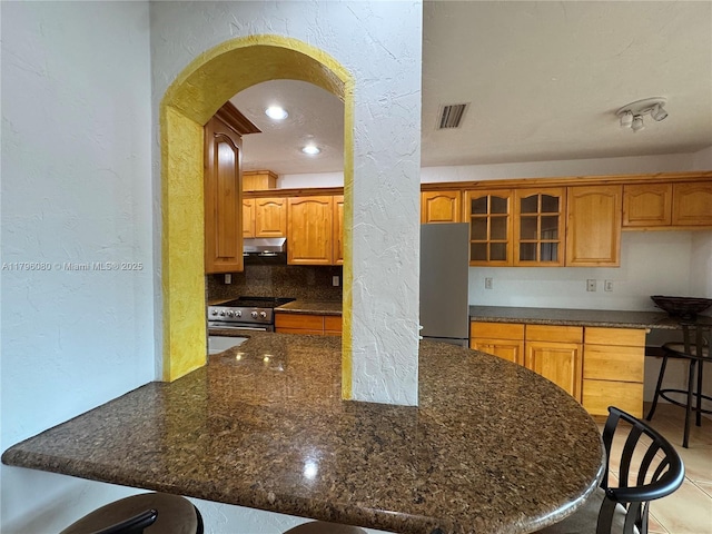 kitchen with arched walkways, a breakfast bar, appliances with stainless steel finishes, and a textured wall