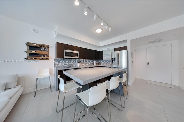 kitchen with a kitchen breakfast bar, light tile patterned flooring, backsplash, a kitchen island, and appliances with stainless steel finishes