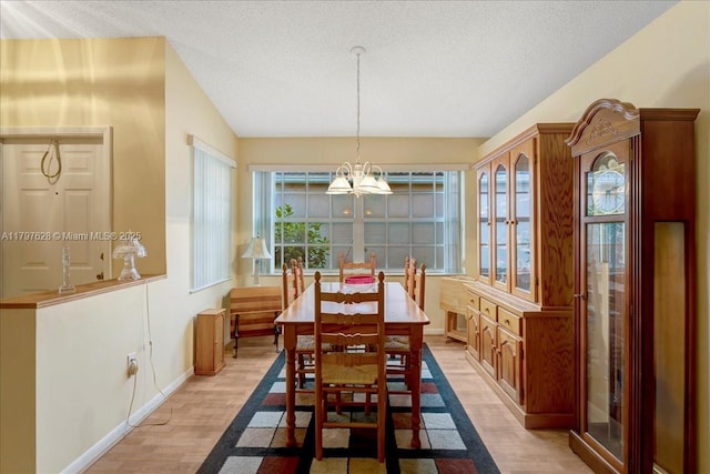 dining room with light wood finished floors, a textured ceiling, baseboards, and a notable chandelier