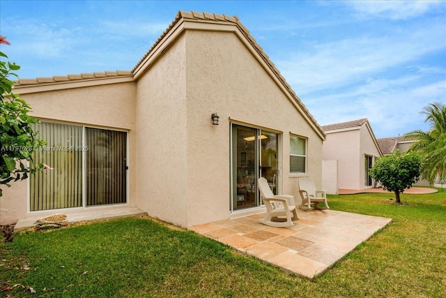 rear view of house with a lawn, a patio, a tiled roof, and stucco siding