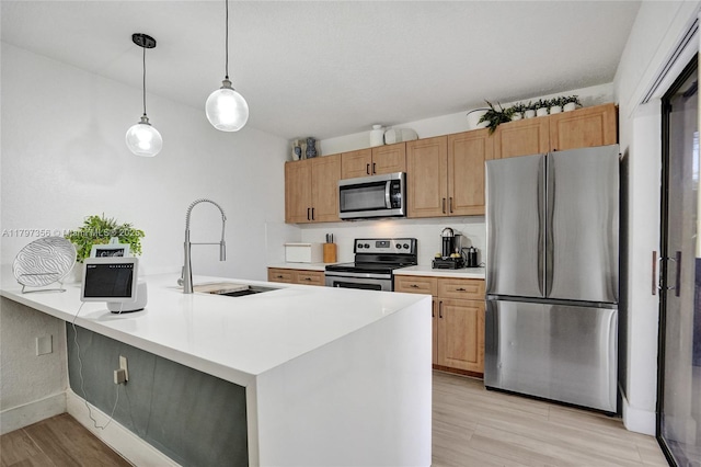 kitchen featuring a peninsula, a sink, stainless steel appliances, light countertops, and light wood-style floors