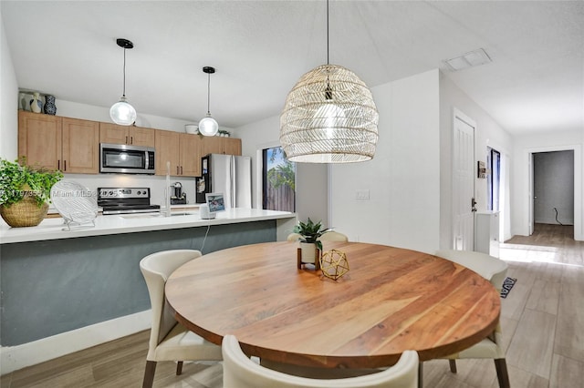dining area featuring baseboards, light wood finished floors, and visible vents