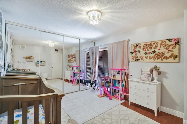 bedroom with a closet, a textured ceiling, baseboards, visible vents, and wood finished floors