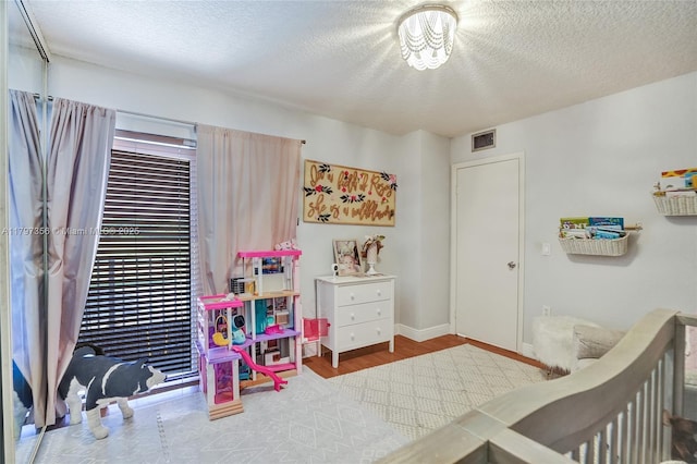 bedroom featuring a textured ceiling, baseboards, visible vents, and wood finished floors