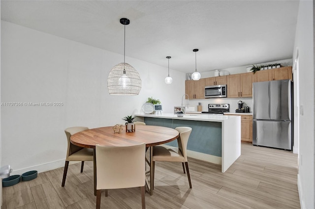 kitchen with stainless steel appliances, pendant lighting, light wood finished floors, light countertops, and baseboards