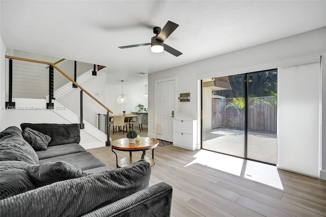 living area featuring visible vents, light wood-style flooring, a ceiling fan, and stairs