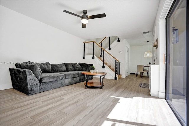 living area featuring stairway, ceiling fan, light wood-type flooring, and visible vents
