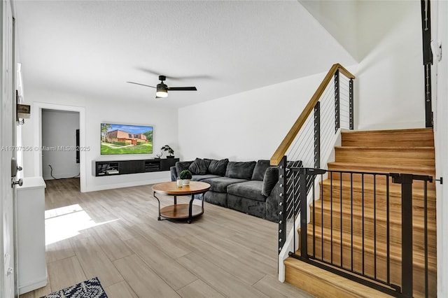 living room featuring light wood-style flooring, a ceiling fan, and stairs