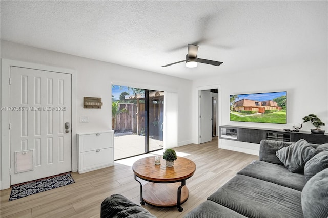 living area with light wood-style floors, baseboards, a ceiling fan, and a textured ceiling
