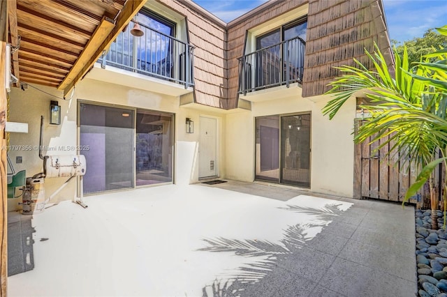 back of property with a patio area, stucco siding, mansard roof, and a balcony