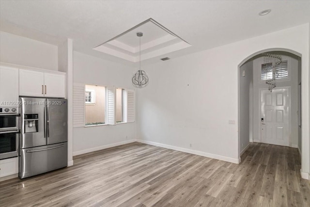 12471 NW 78th Mnr, Parkland, FL 33076 - unfurnished dining area with arched walkways, a tray ceiling, baseboards, light wood-style flooring, and healthy amount of natural light