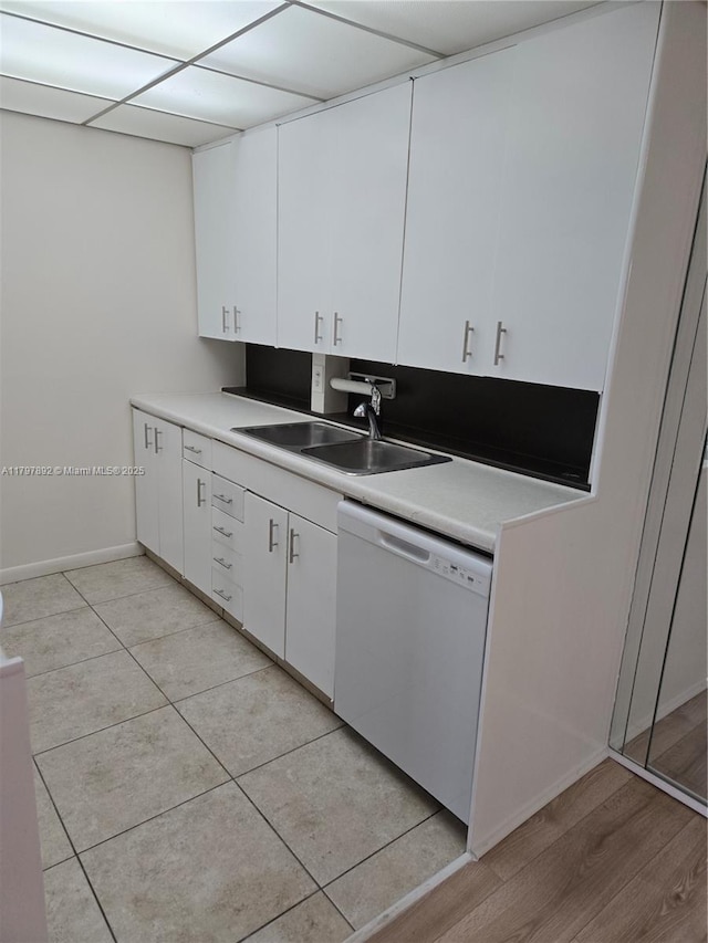 kitchen with a sink, dishwasher, white cabinetry, light countertops, and baseboards