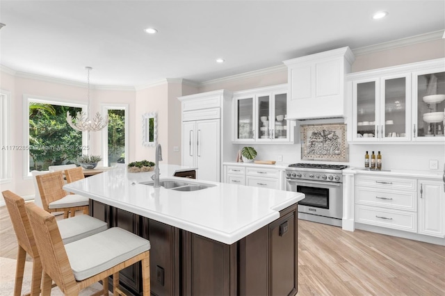 kitchen featuring a sink, an island with sink, white cabinetry, high quality appliances, and light countertops