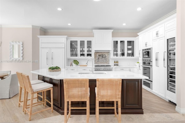 kitchen featuring a sink, a kitchen bar, crown molding, light wood-style floors, and appliances with stainless steel finishes