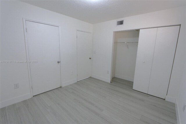 unfurnished bedroom featuring light wood-type flooring, baseboards, visible vents, and a textured ceiling