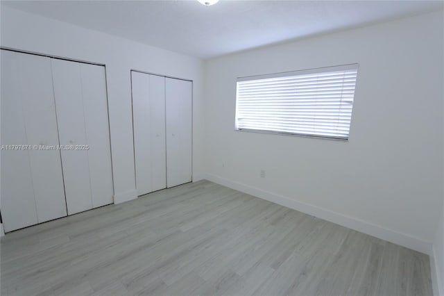 unfurnished bedroom featuring baseboards, light wood-style floors, and multiple closets