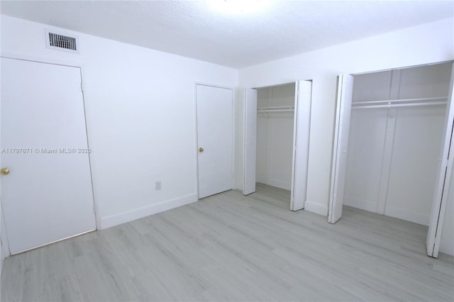 unfurnished bedroom featuring baseboards, visible vents, two closets, and wood finished floors