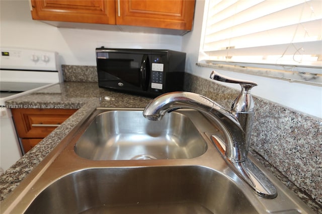 details featuring a sink, stove, brown cabinetry, and black microwave