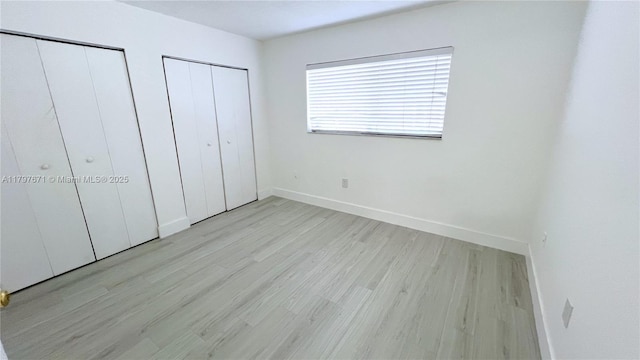 unfurnished bedroom with baseboards, multiple closets, and wood finished floors