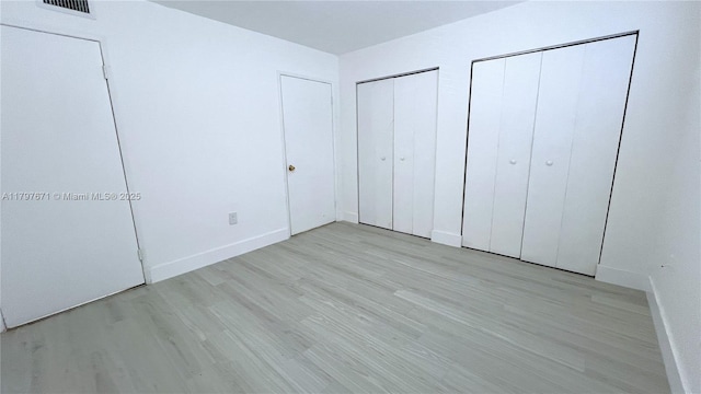 unfurnished bedroom with visible vents, light wood-style flooring, baseboards, and multiple closets