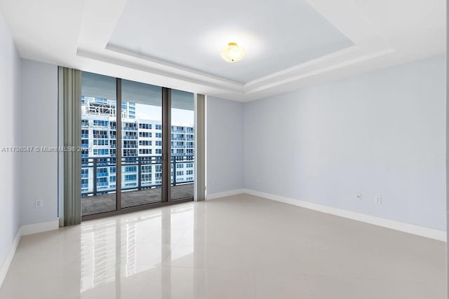 unfurnished room with baseboards, a raised ceiling, light tile patterned floors, and a wall of windows