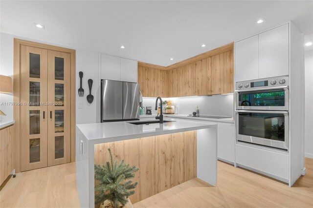 7560 SW 144th St, Palmetto Bay, FL 33158 - kitchen featuring a sink, an island with sink, light wood finished floors, modern cabinets, and appliances with stainless steel finishes
