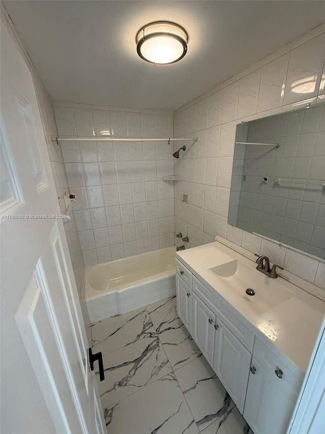 full bath with marble finish floor, tile walls, vanity, and shower / washtub combination