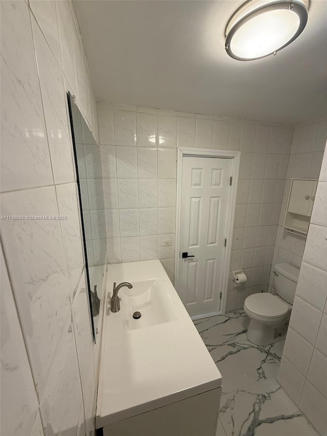 bathroom with tile walls, toilet, marble finish floor, and vanity
