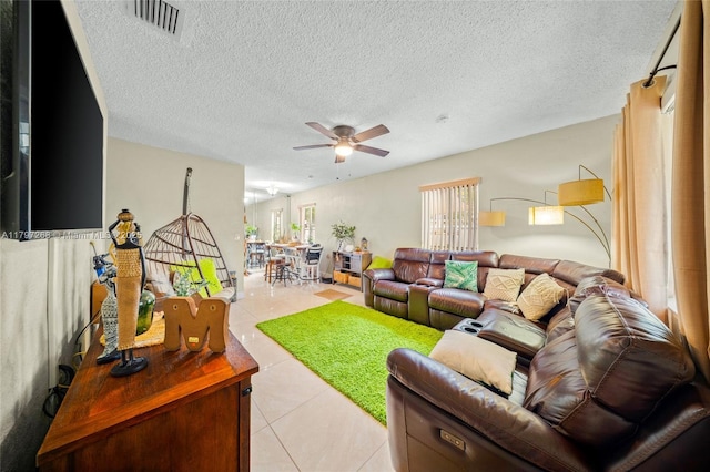 living room featuring a textured ceiling, visible vents, light tile patterned flooring, and ceiling fan