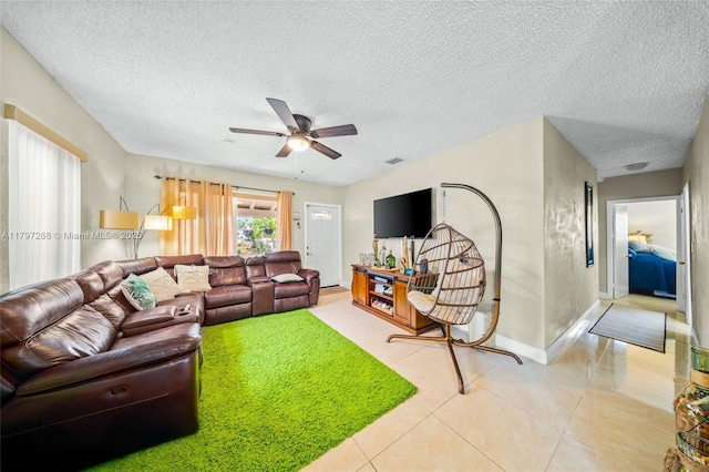 living area featuring a ceiling fan, a textured ceiling, baseboards, light tile patterned floors, and visible vents
